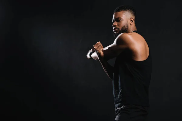 Vista lateral del atlético joven afroamericano hombre estiramiento músculos aislados en negro - foto de stock