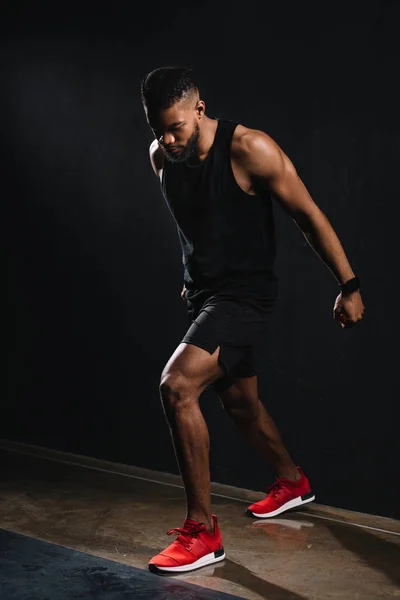 Vista completa de la musculosa joven afroamericano hombre en ropa deportiva ejerciendo sobre negro - foto de stock