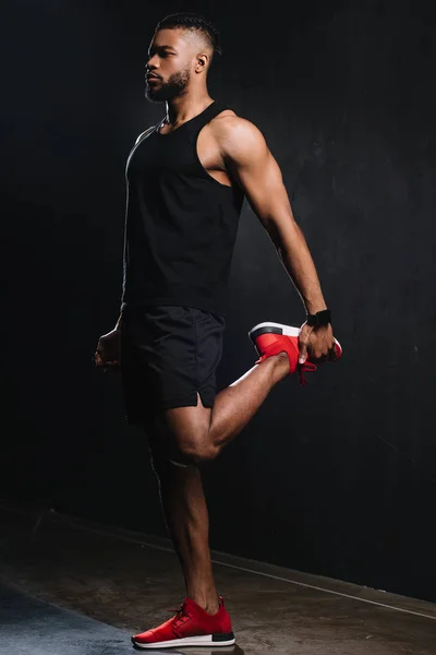 Full length view of young african american sportsman stretching muscles on black — Stock Photo