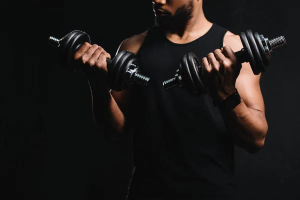 Tiro recortado do homem americano africano muscular exercitando com halteres isolados em preto — Fotografia de Stock