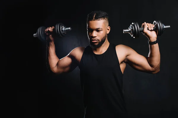 Красивый мускулистый африканский американец, тренирующийся с гантелями на черном — стоковое фото