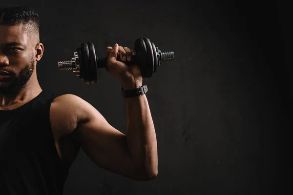 Cropped shot of muscular african american man training with dumbbell isolated on black — Stock Photo