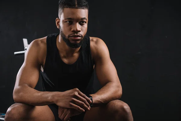 Handsome young african american sportsman sitting and looking away on black — Stock Photo