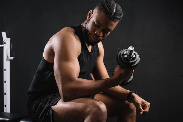 Muscoloso giovane uomo africano americano che si esercita con i manubri sul nero — Foto stock