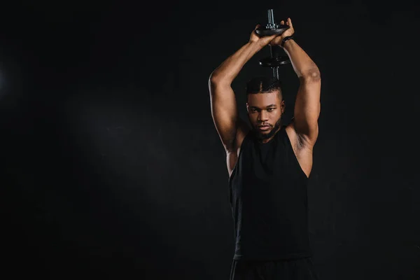 Спортивний молодий афроамериканський чоловік займається з гантелі ізольовані на чорному — стокове фото