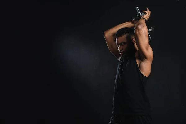 Musculoso joven afroamericano deportista ejercicio con mancuerna aislado en negro - foto de stock