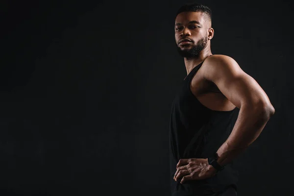 Side view of athletic young african american man in sportswear looking at camera isolated on black — Stock Photo