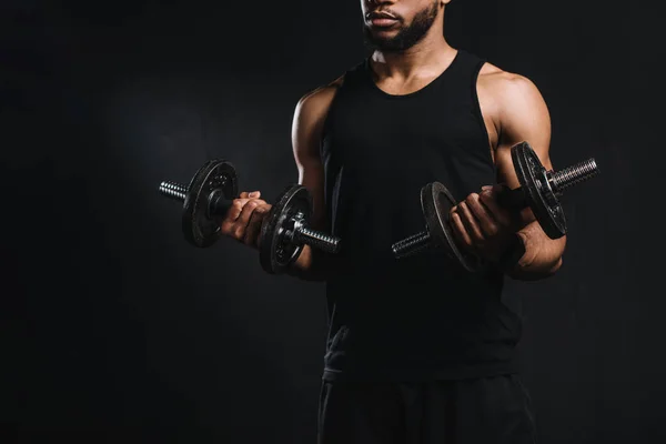 Обрезанный кадр мускулистого африканского американца, тренирующегося с гантелями, изолированными на черном — стоковое фото