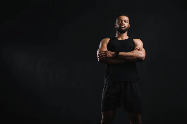 Vue à faible angle de sportif afro-américain confiant debout avec les bras croisés et regardant la caméra isolée sur noir — Photo de stock