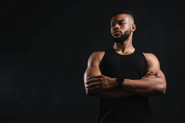 Vue à faible angle de sportif afro-américain confiant debout avec les bras croisés et regardant loin isolé sur noir — Photo de stock