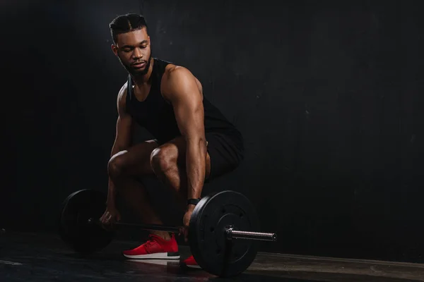 Full length view of young african american sportsman lifting barbell on black — Stock Photo