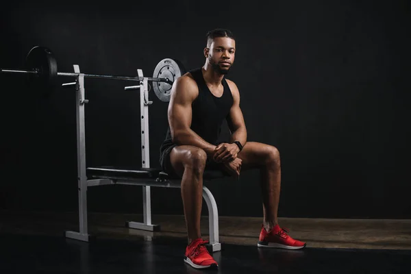 Muskulöser junger afrikanisch-amerikanischer Mann in Sportbekleidung, der im Fitnessstudio vor der Kamera sitzt — Stockfoto