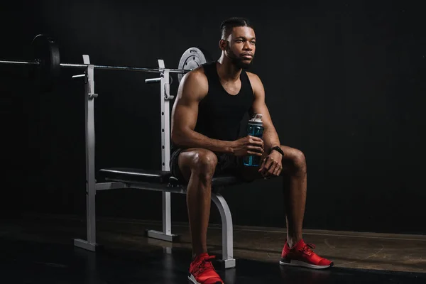 Junger afrikanisch-amerikanischer Sportler hält eine Flasche Wasser in der Hand und schaut weg auf schwarz — Stockfoto