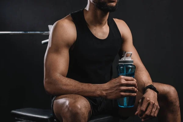 Cropped shot of muscular african american sportsman sitting and holding bottle of water — Stock Photo