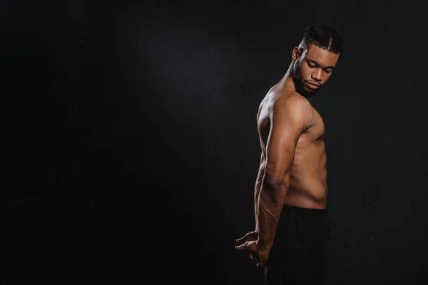 Vue latérale de musclé jeune homme afro-américain étirant les mains isolé sur noir — Photo de stock