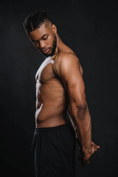 Side view of shirtless muscular young african american man stretching hands isolated on black — Stock Photo