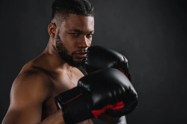 Joven boxeador afroamericano sin camisa en guantes de boxeo mirando a la cámara aislada en negro - foto de stock
