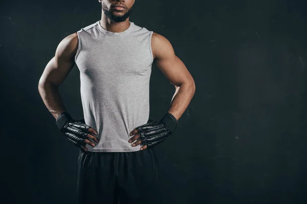 Cropped shot of muscular african american kickboxer in gloves standing with hands on waist isolated on black — Stock Photo