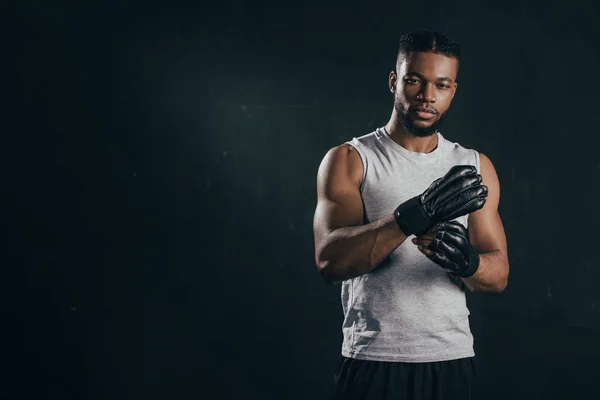 Young african american kickboxer wearing gloves and looking at camera isolated on black — Stock Photo