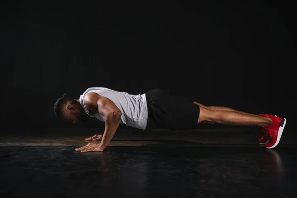 Seitenansicht eines jungen afrikanisch-amerikanischen Sportlers, der Liegestütze auf schwarz macht — Stockfoto