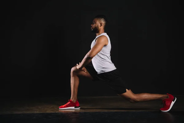 Vista lateral do atlético jovem afro-americano em sportswear exercitando e olhando para o preto — Fotografia de Stock