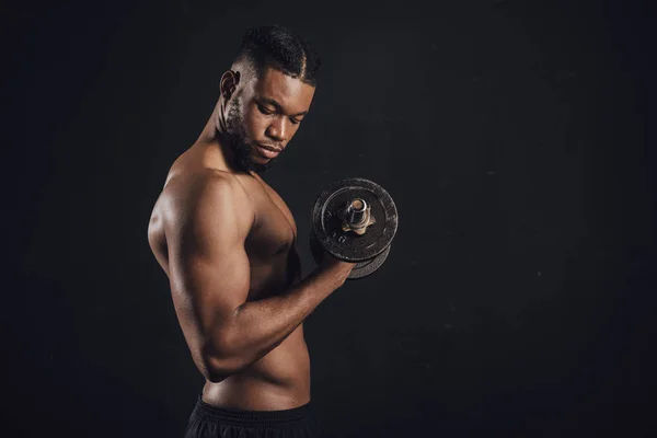 Seitenansicht des muskulösen, hemdlosen afrikanisch-amerikanischen Mannes, der mit einer Hantel isoliert auf schwarz trainiert — Stockfoto