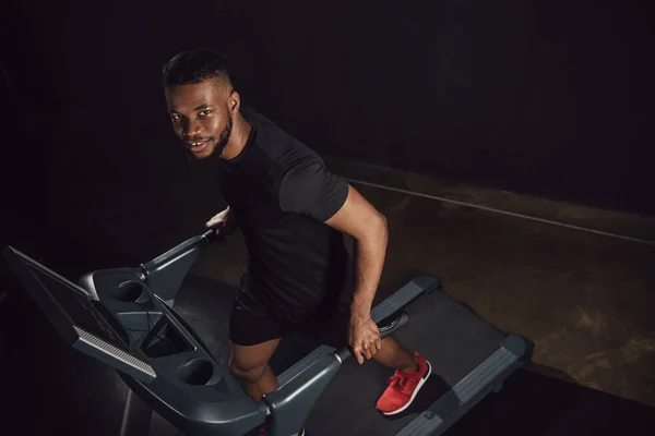 Hochblickaufnahme eines jungen afrikanisch-amerikanischen Sportlers, der auf dem Laufband trainiert und in die Kamera blickt — Stockfoto