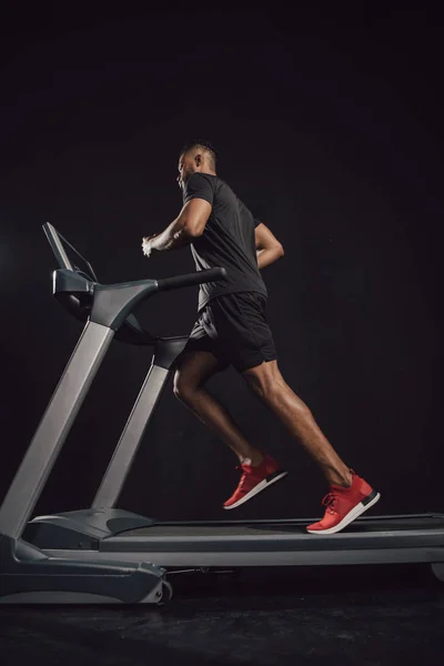 Vue à faible angle du jeune sportif afro-américain courant sur tapis roulant sur noir — Photo de stock