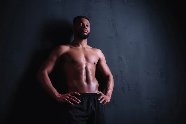 Tiefansicht eines muskulösen, hemdlosen jungen Mannes, der mit den Händen auf der Taille steht und wegschaut auf schwarz — Stockfoto