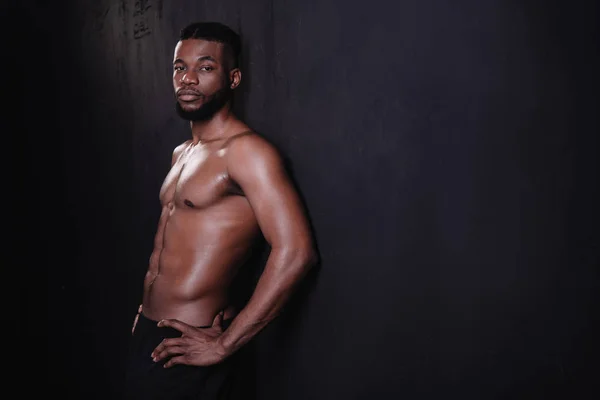 Bonito sem camisa muscular jovem afro-americano homem olhando para câmera no preto — Fotografia de Stock