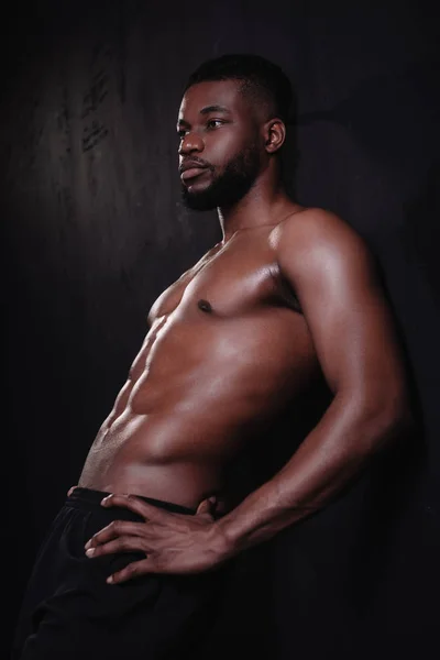 Muscular shirtless young african american man standing with hands on waist and looking away on black — Stock Photo