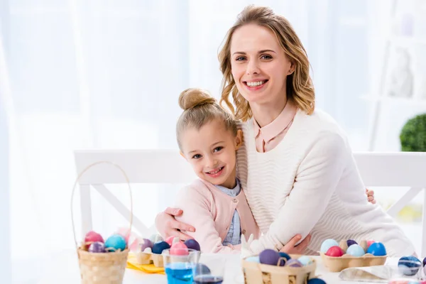 Мати і дочка обіймаються за столом з розфарбованими великодніми яйцями — стокове фото