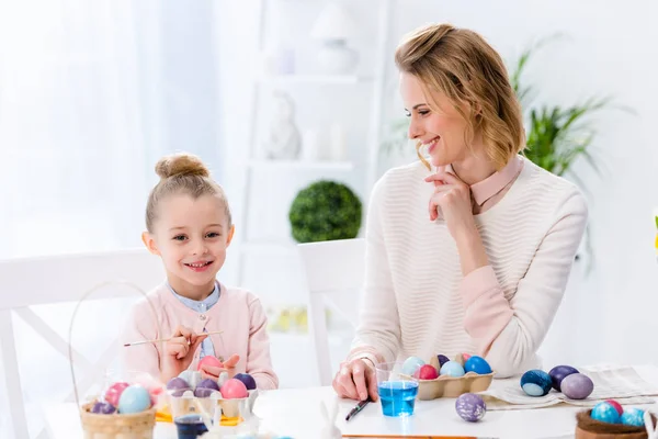 Mujer joven y niña pintando huevos de Pascua - foto de stock