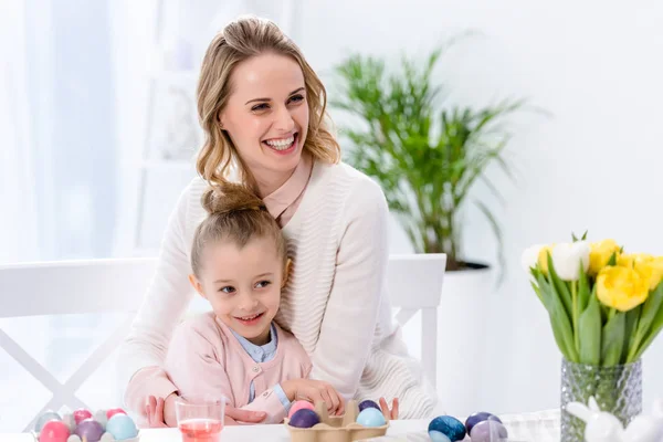 Cheerful mother and daughter by table with painted eggs on Easter — Stock Photo