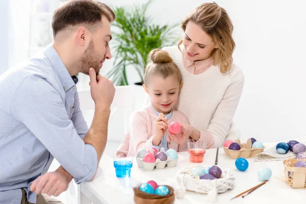 Родители и дочь рисуют пасхальные яйца разных цветов — стоковое фото