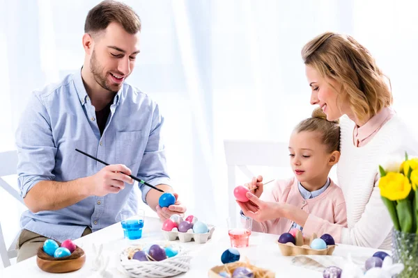 Family coloring Easter eggs with painting brushes — Stock Photo