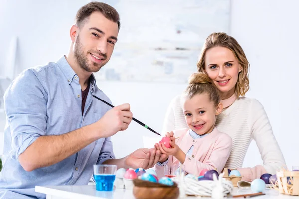 Padre e hija sonriendo mientras pintan huevos de Pascua - foto de stock