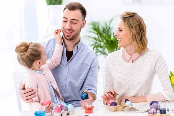 Familia e hija se divierten mientras pintan huevos para Pascua - foto de stock
