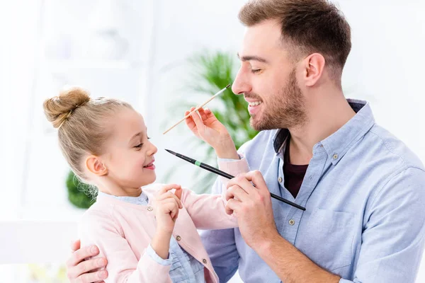 Father and daughter having fun with paint brushes — Stock Photo