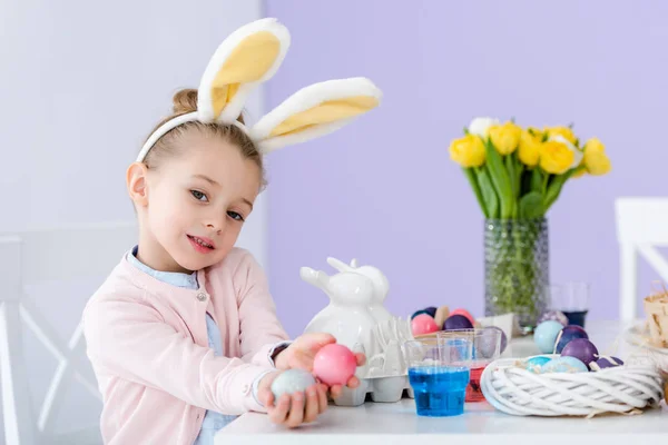 Ragazzo in orecchie di coniglio che mostra uova colorate per Pasqua — Foto stock