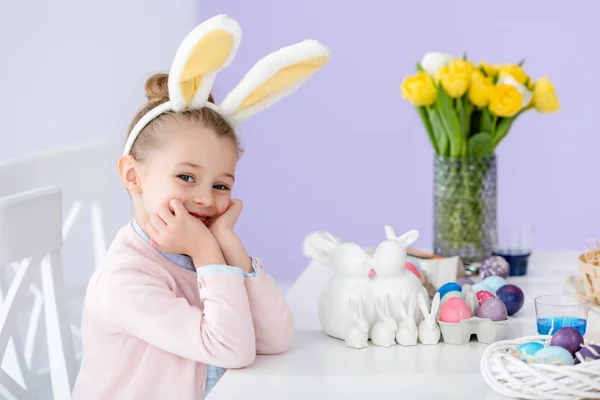 Niño en orejas de conejo por mesa con huevos de Pascua - foto de stock
