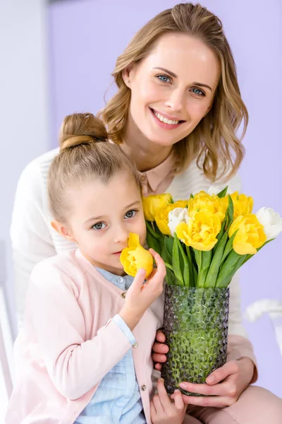 Atractiva joven mujer y niño sosteniendo jarrón con tulipanes en el día de la mujer - foto de stock