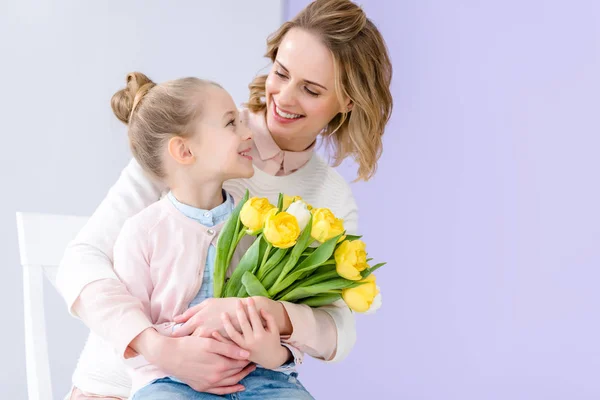 Cute child embracing mother with tulips bouquet on 8 march — Stock Photo