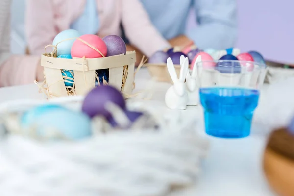Vista de cerca de los huevos de Pascua de colores y pintura en la mesa delante de los niños y los padres - foto de stock