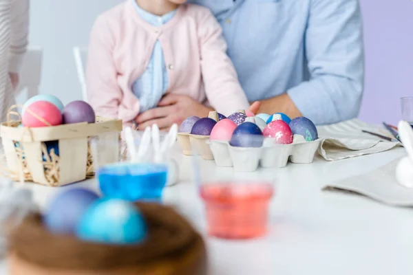 Painted Easter eggs on table in front of child and parents — Stock Photo