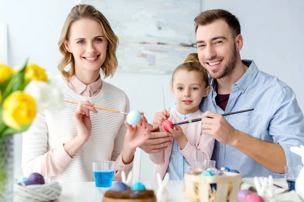 Celebrando familia con hija para colorear huevos de Pascua por mesa - foto de stock