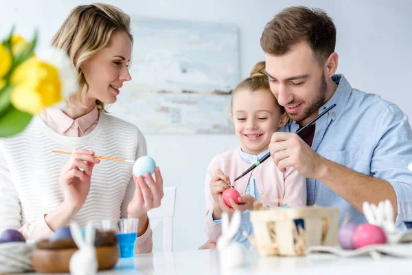 Familia sonriente con hija para colorear huevos de Pascua de pollo - foto de stock