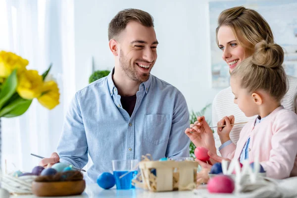 Lächelnde Familie beim Osterspaß am Tisch mit bemalten Eiern — Stockfoto