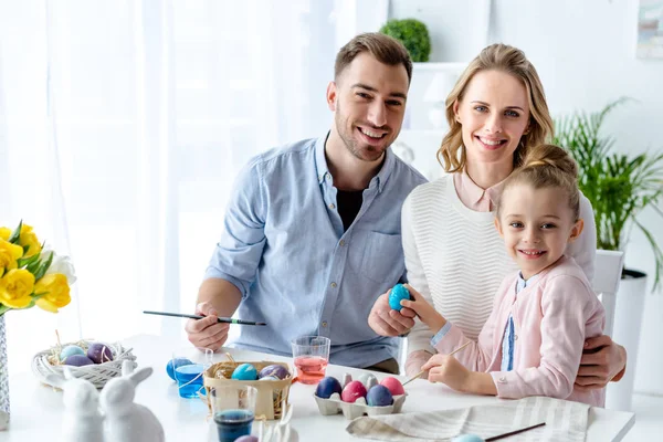 Улыбающаяся семья с дочерью, раскрашивающей пасхальные яйца — стоковое фото