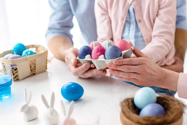 Cartonagem com ovos de Páscoa coloridos em mãos de família com filha — Fotografia de Stock
